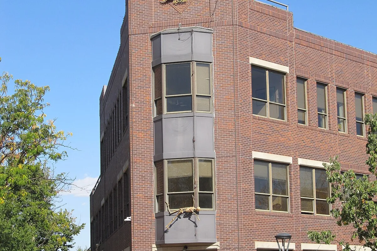 The brick corner building of Old Town Square in Fort Collins, its star-topped gable and bay windows above a shopfront, planters in bloom below