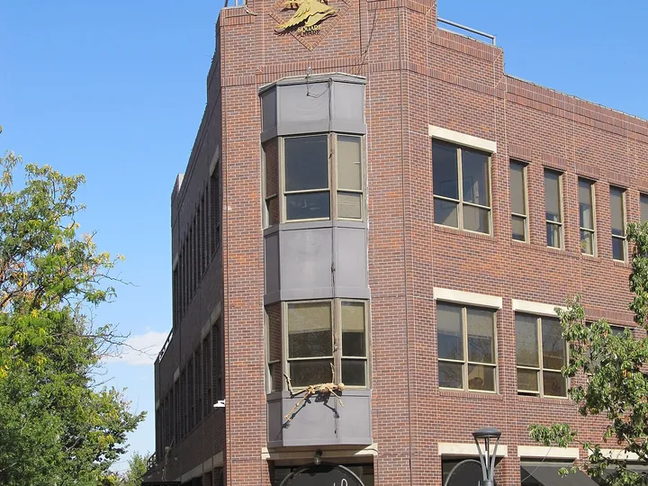 The brick corner building of Old Town Square in Fort Collins, its star-topped gable and bay windows above a shopfront, planters in bloom below